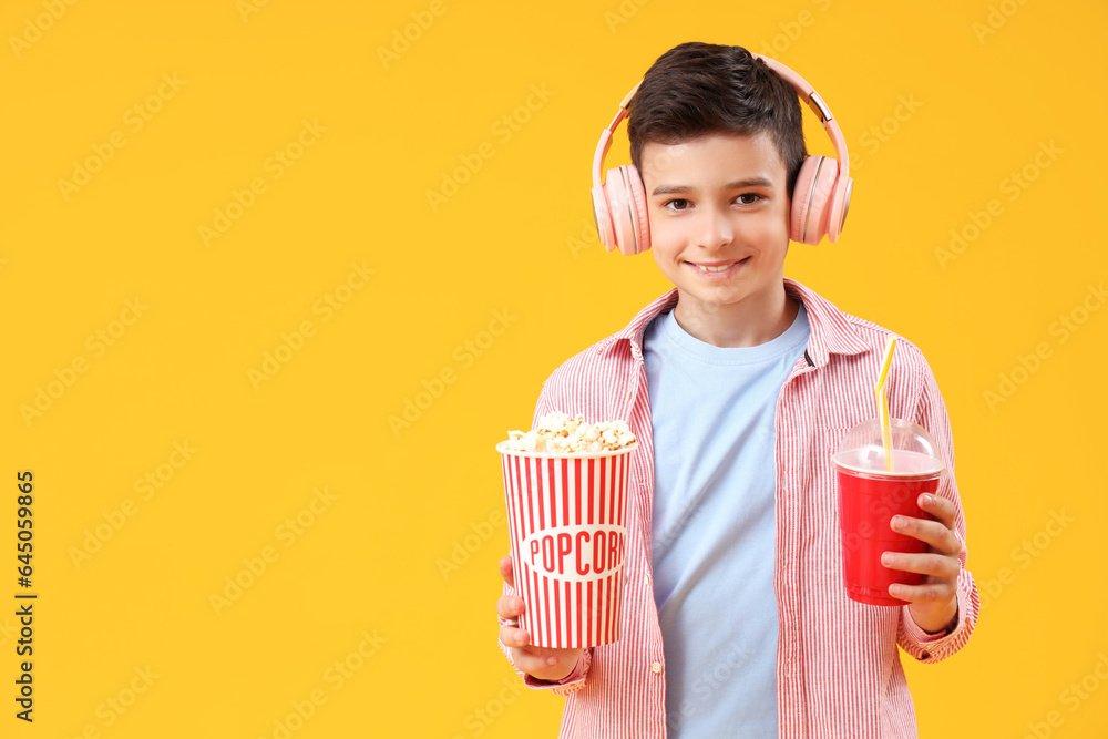 Cute little boy in headphones with popcorn and drink on orange background