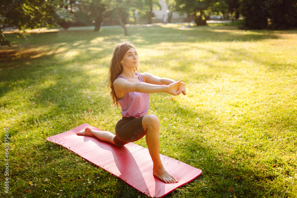 Fitness woman doing yoga, sports exercises in the park. Athletic woman sitting on a mat outdoors on 