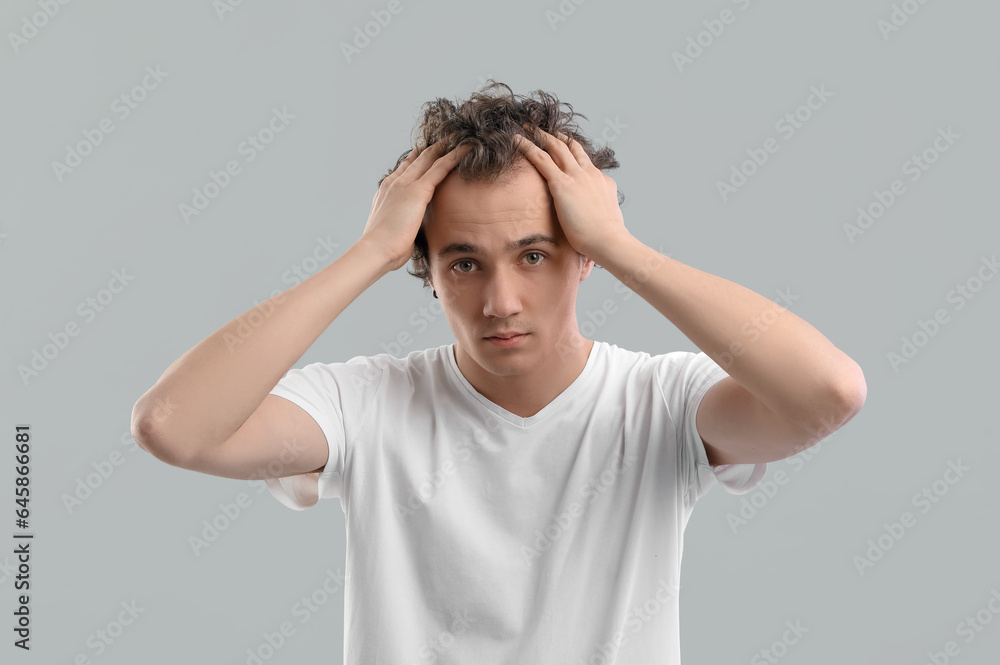 Young man with hair loss problem on grey background