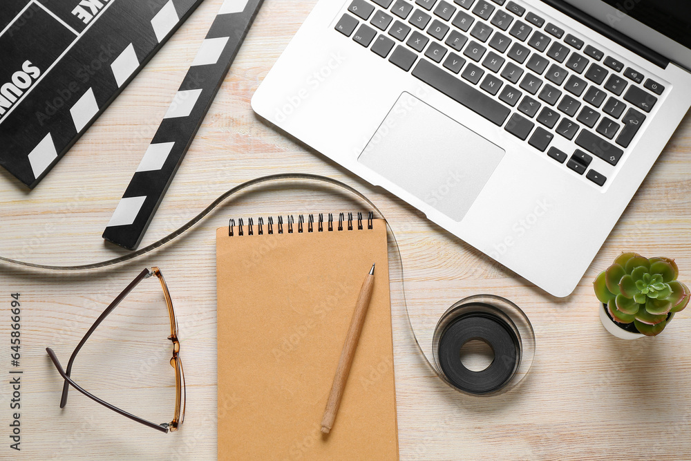 Notebook with film, movie clapper and laptop on light wooden background