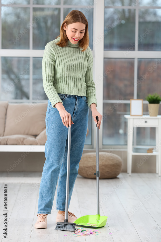 Young woman sweeping floor in room