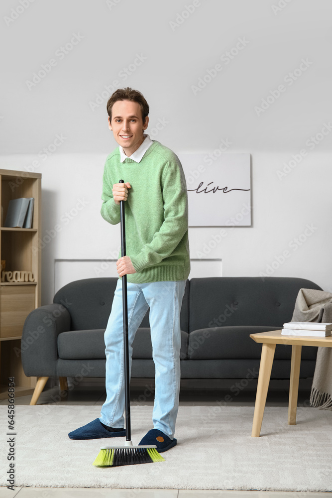 Young man sweeping carpet with broom at home