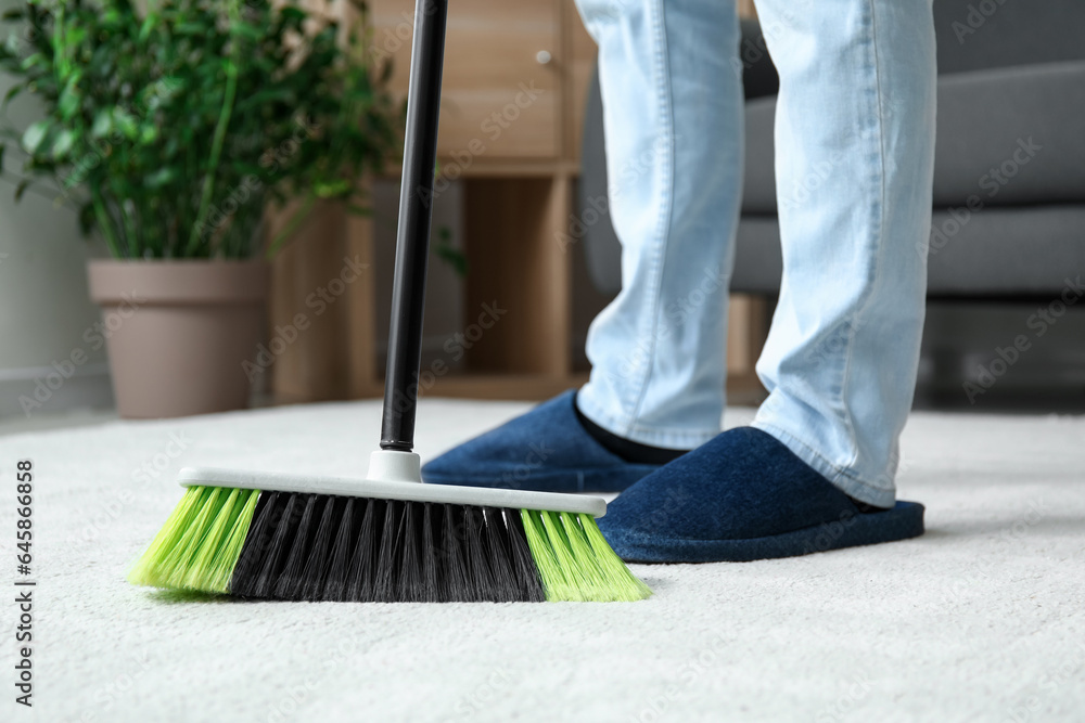 Young man sweeping carpet with broom at home, closeup