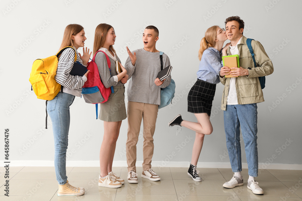 Group of students and their kissing friends near grey wall