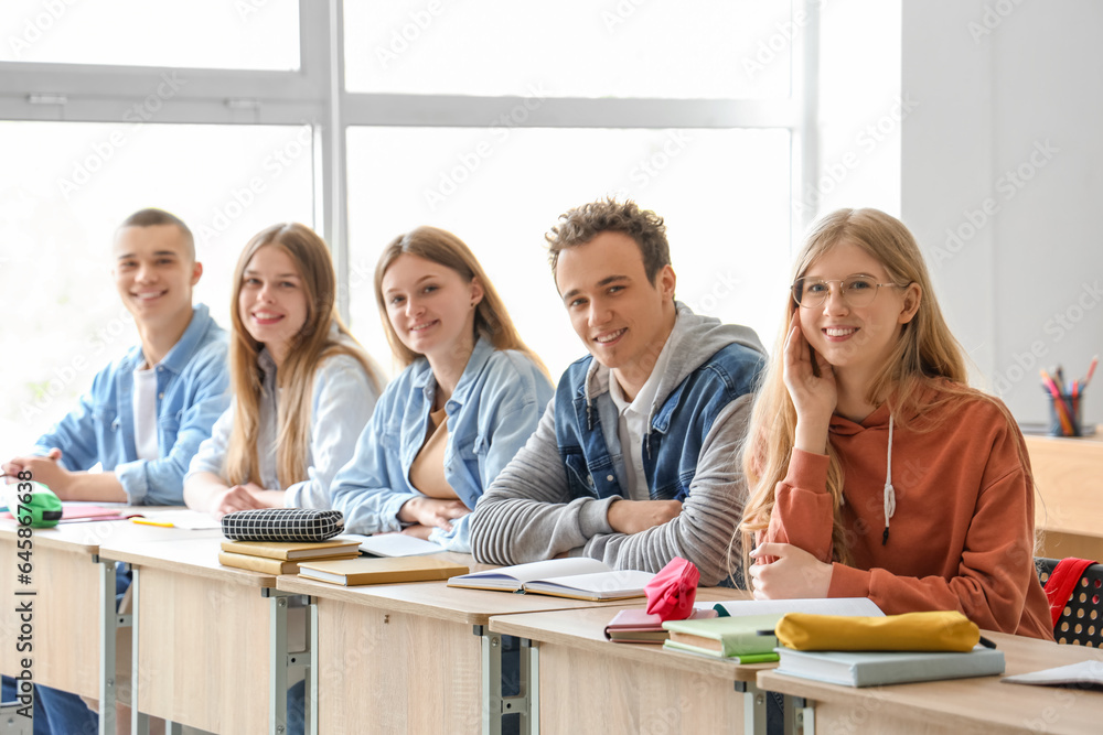 Happy classmates sitting at desks in classroom