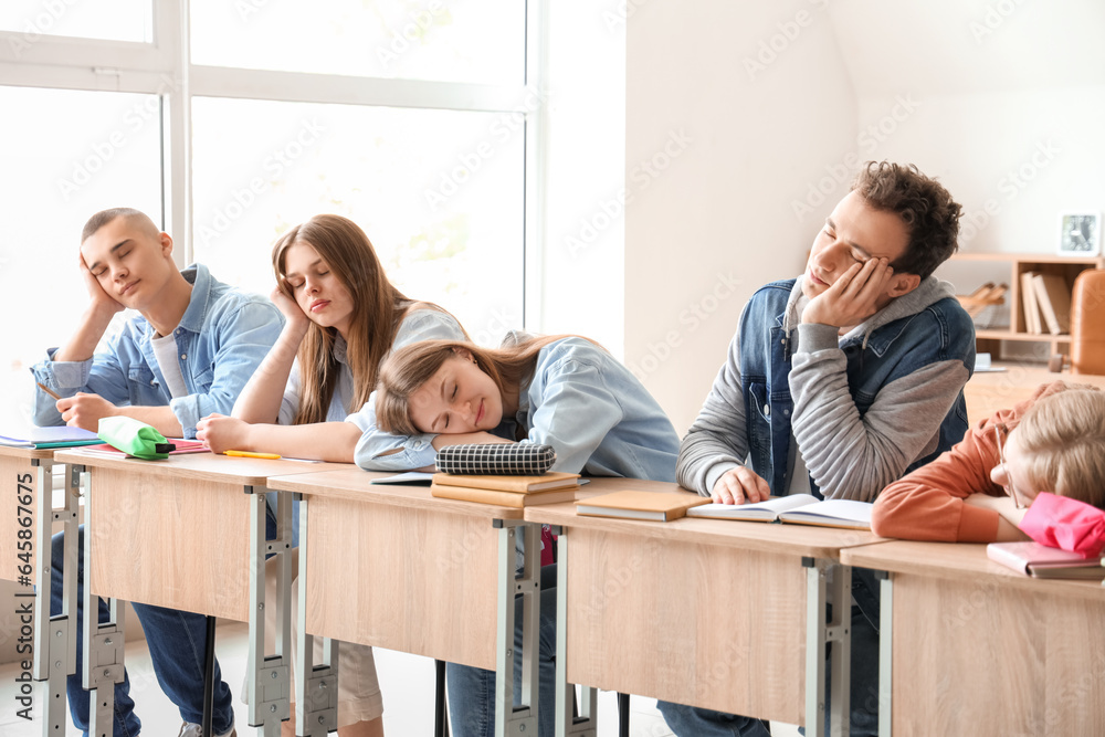 Tired sleepy classmates sitting at desks in classroom