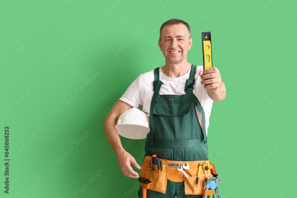 Mature builder with level and hardhat on green background