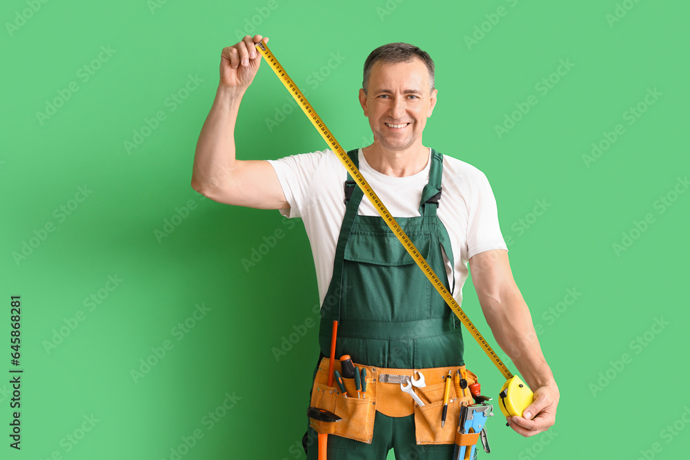 Mature builder with tape measure on green background