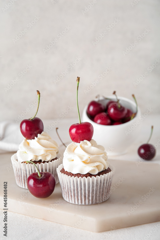 Board with tasty cherry cupcakes on light background