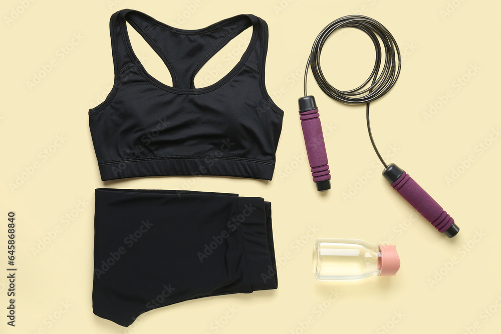 Sportswear, skipping rope and bottle of water on color background