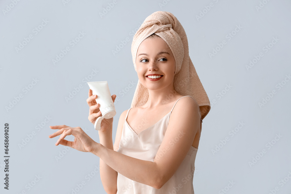 Pretty young woman after shower applying lotion against light background