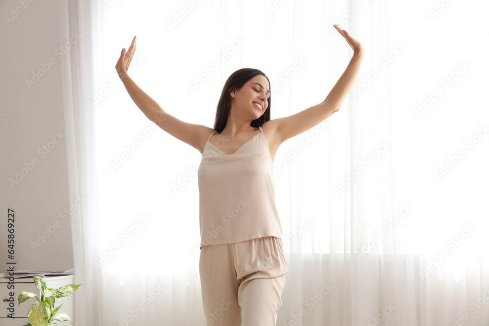 Morning of beautiful young woman in pajamas near window