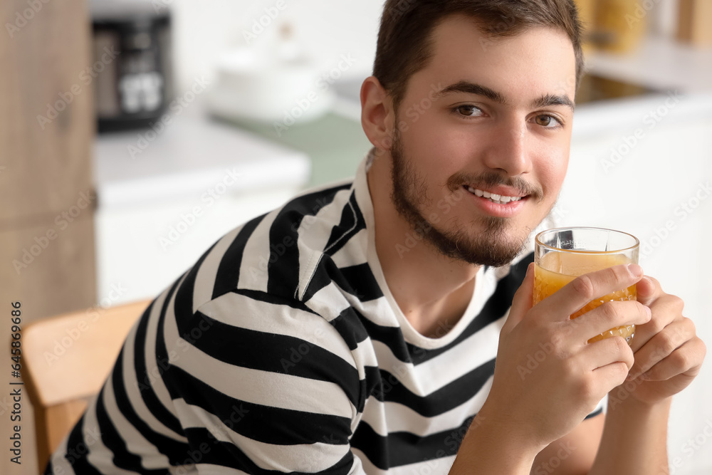 Young man with glass of juice in kitchen, closeup