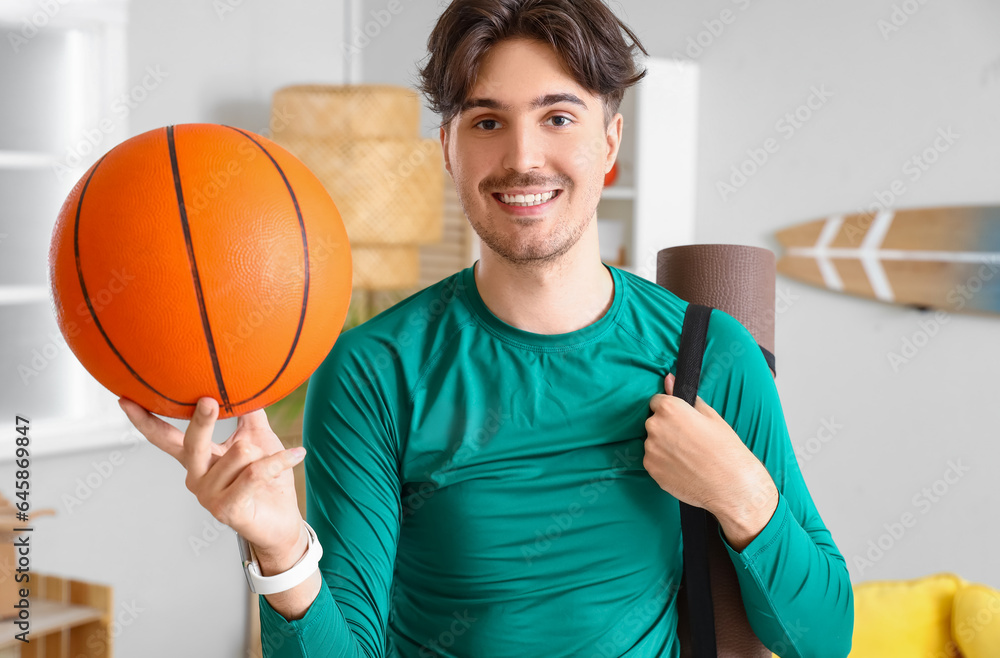 Sporty young man with yoga mat and ball at home