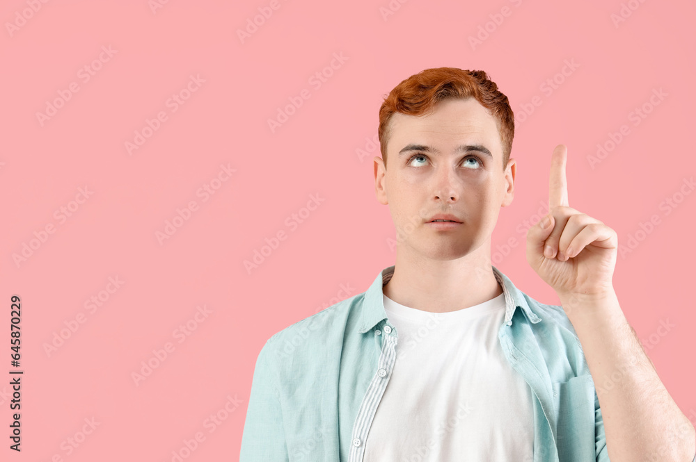 Thoughtful young redhead man pointing at something on pink background