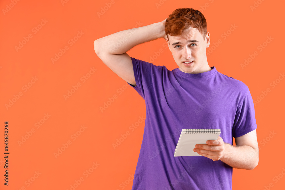 Thoughtful young redhead man with notebook on orange background