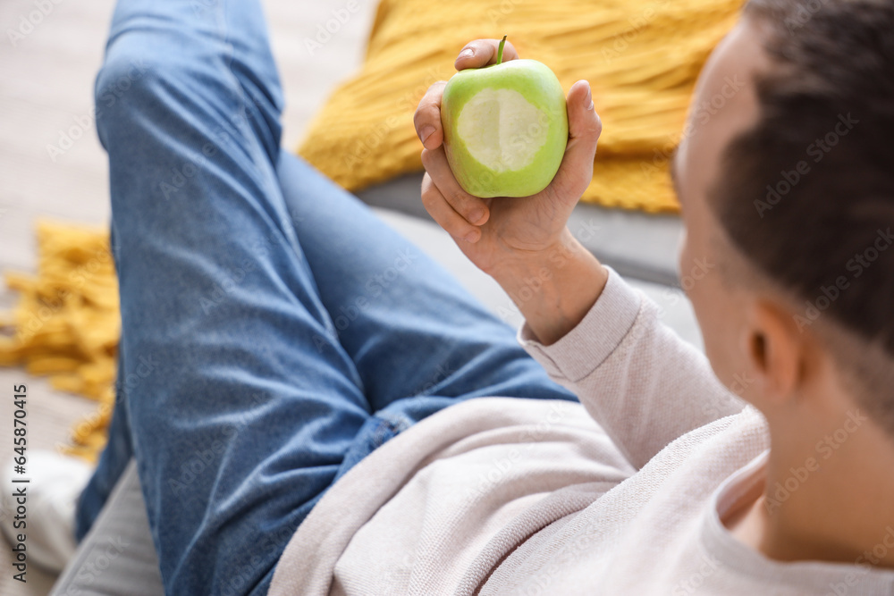 Young man with tasty apple at home, closeup