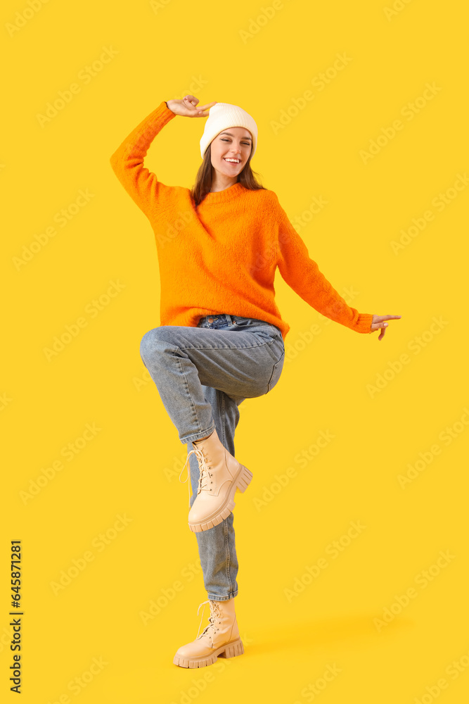 Happy young woman in winter clothes on yellow background