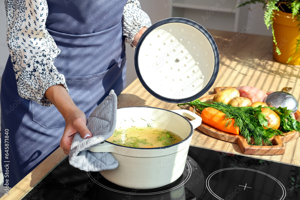 Young woman cooking chicken soup on stove in kitchen, closeup