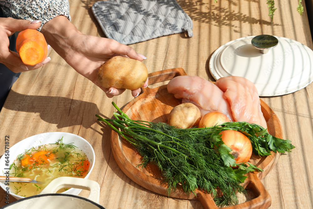 Young woman with ingredients for chicken soup in kitchen, closeup