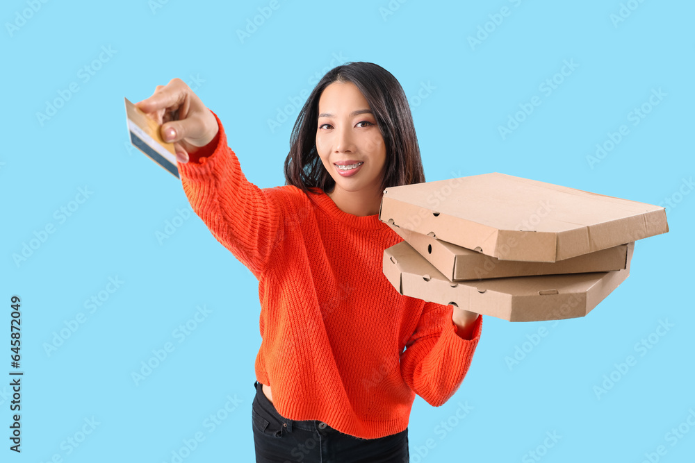 Young Asian woman with credit card and pizza boxes on blue background