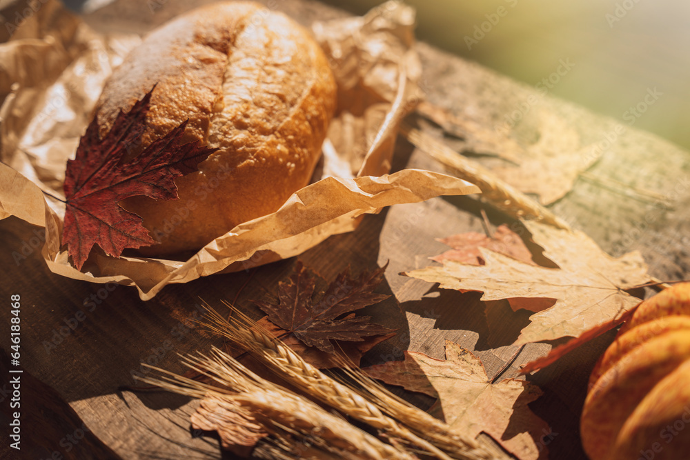 Fresh loaf of bread in paper packaging with maple leaves on a wooden table.