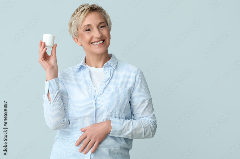 Mature woman with jar of cream on light background