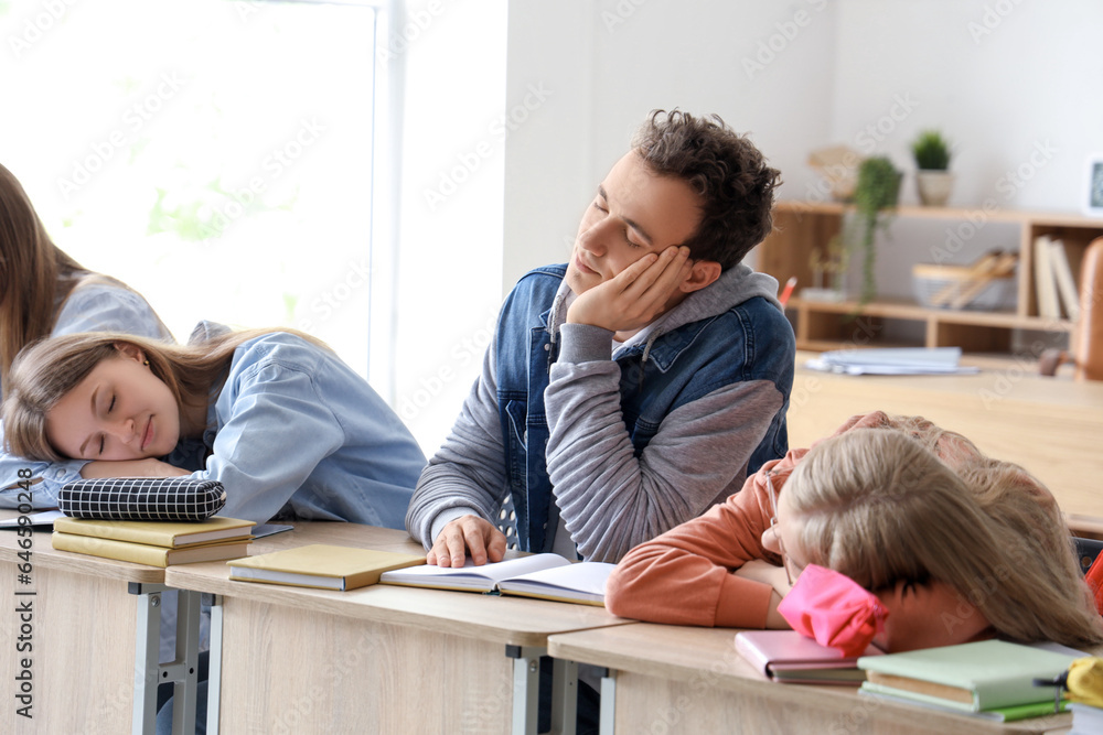 Tired sleepy classmates sitting at desks in classroom