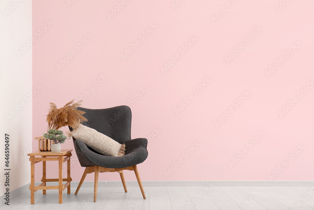 Grey armchair and vase with pampas grass on coffee table near pink wall