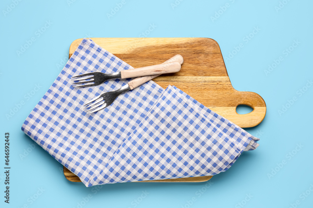 Wooden cutting board, cutlery and napkin on color background