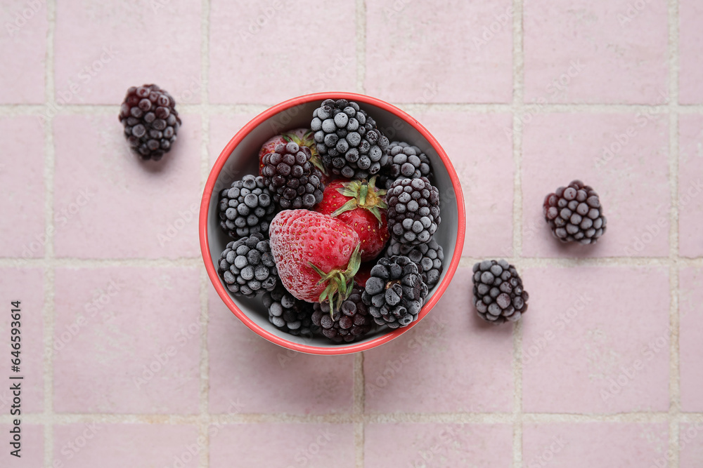 Bowl of frozen berries on color tile background