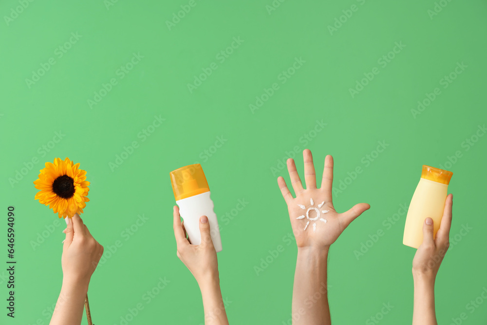 Female hands with bottles of sunscreen cream and sunflower on green background