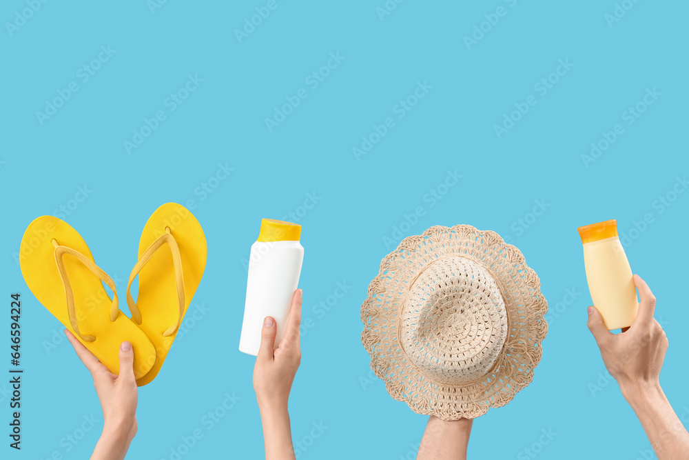 Female hands with bottles of sunscreen cream, hat and flip flops on blue background