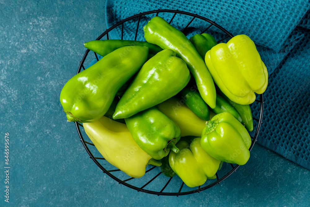 Basket with different fresh peppers on blue background