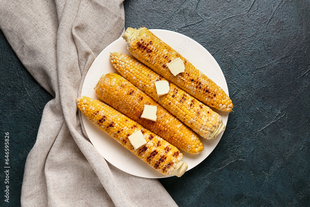 Plate of tasty grilled corn cobs with butter on dark background