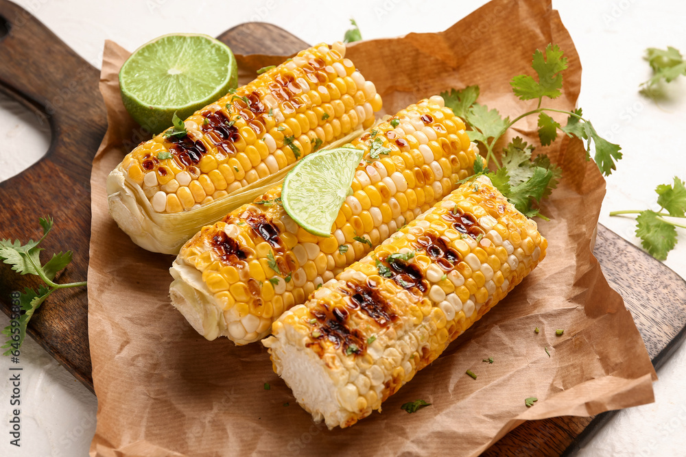 Baking paper with tasty grilled corn cobs and lime on white background