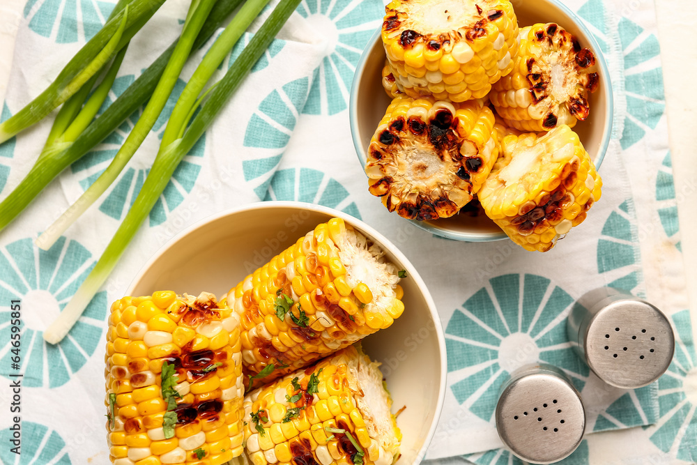 Bowls with tasty grilled corn cobs and green onion on white background