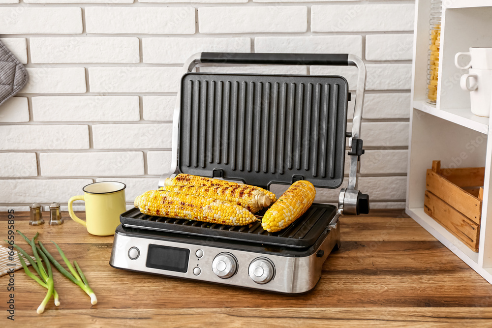 Electric grill with tasty corn on wooden kitchen counter