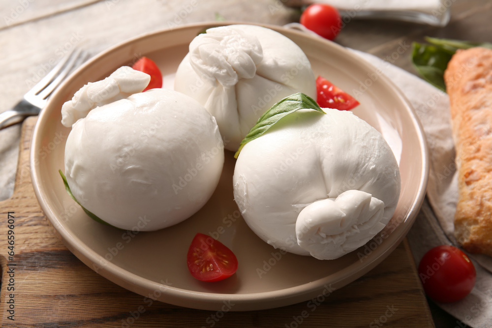 Plate of tasty Burrata cheese with basil and tomatoes on wooden background