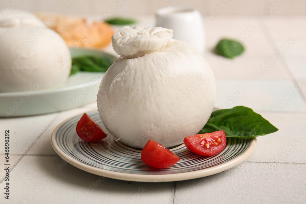 Plate of tasty Burrata cheese with basil and tomatoes on white tile table