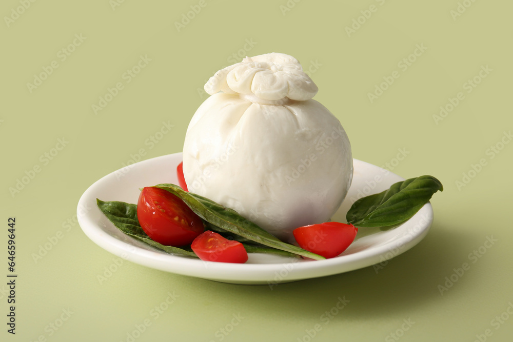 Plate of tasty Burrata cheese with basil and tomatoes on green background