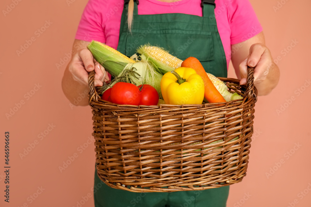 Mature female farmer with wicker basket full of different ripe vegetables on orange background