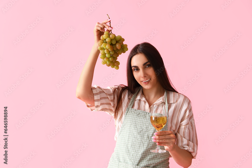 Young woman with glass of wine and grapes on pink background