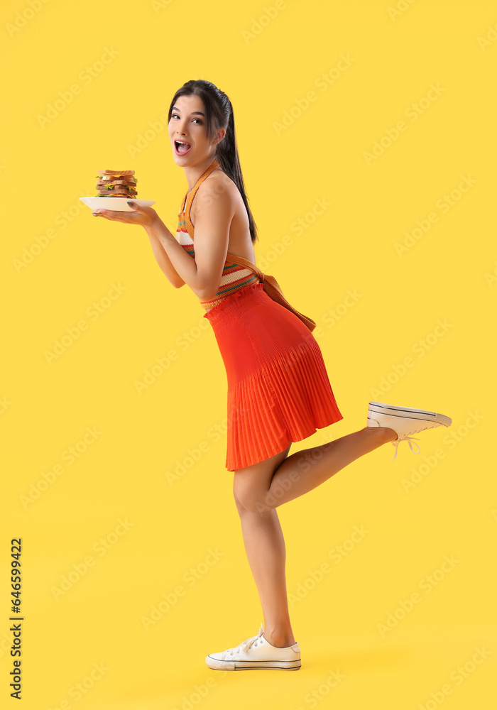 Young woman with tasty sandwich on yellow background