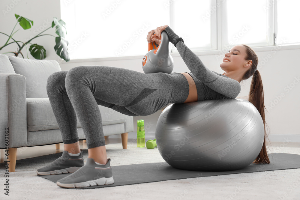 Sporty young woman training with kettlebell and fitball at home