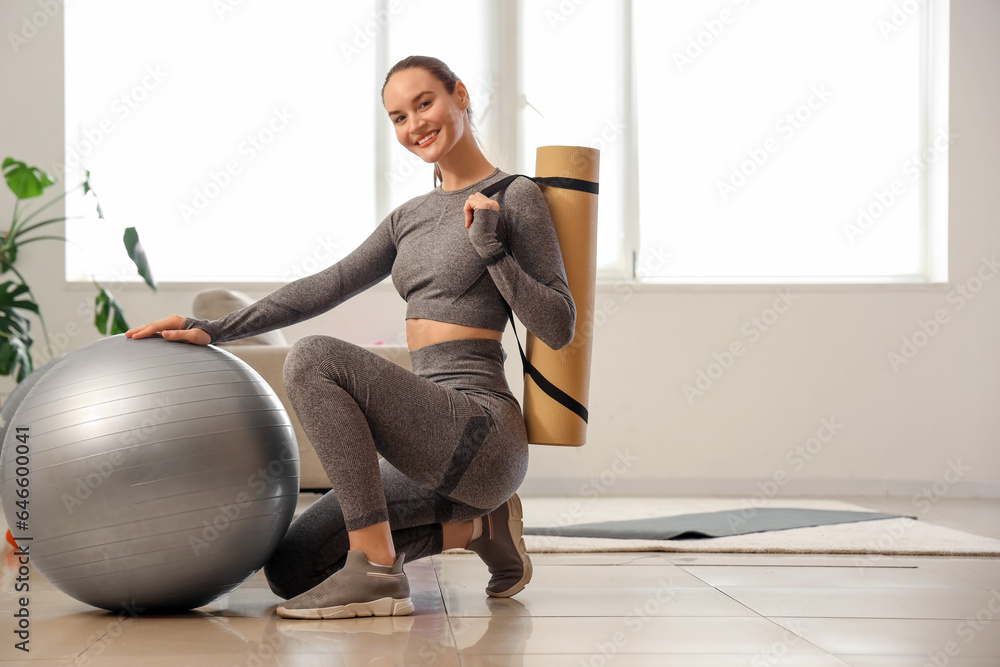 Sporty young woman with mat and fitball at home