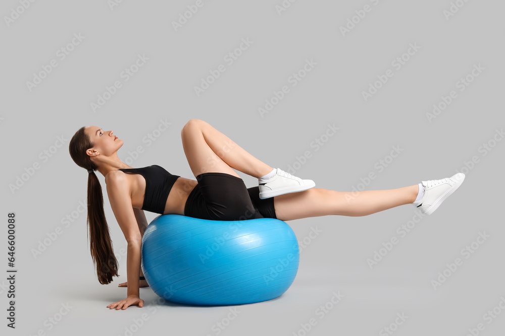 Sporty young woman training with fitball on light background