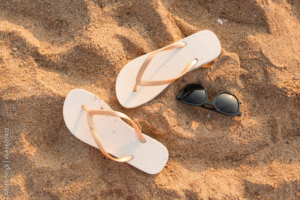 Stylish flips flops with sunglasses on sand at resort