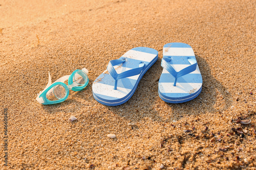 Stylish flips flops with goggles on sand at resort