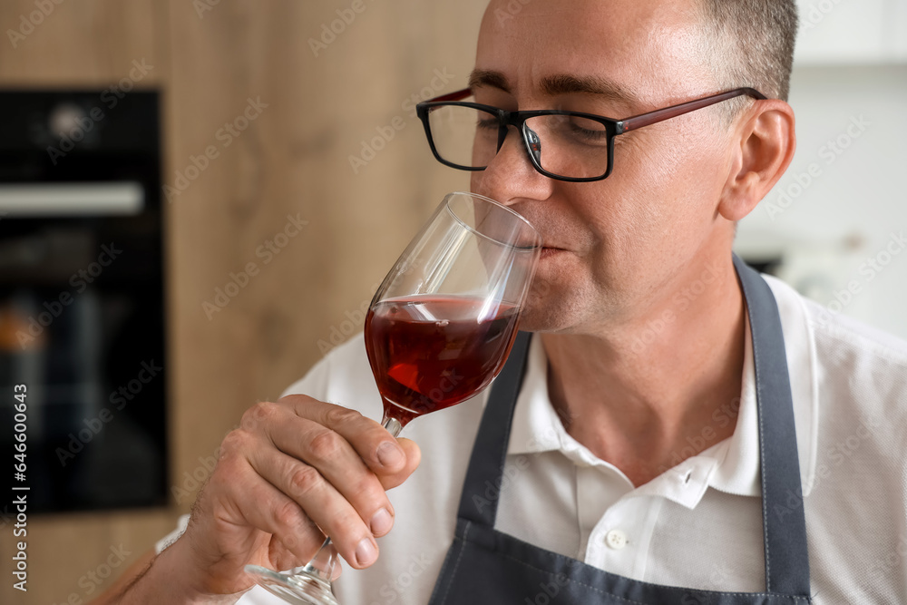 Mature man tasting red wine in kitchen, closeup